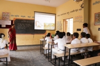 A teacher using digital content on a projector screen in a government school classroom