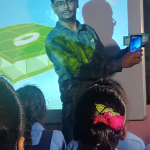 A teacher conducts a lesson using a projector and screen in a smart classroom at GHS MG Dibba School, Chitradurga, Karnataka