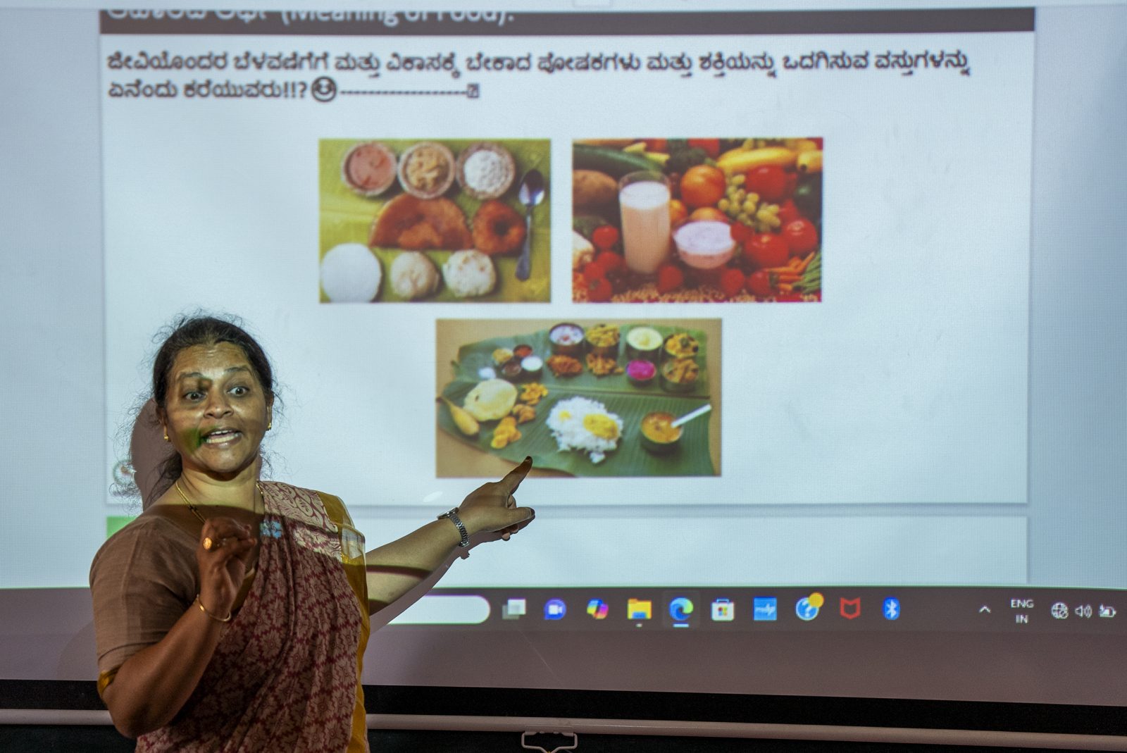 A teacher conducts a lesson using a projector and screen in a smart classroom at GHS MG Dibba School, Chitradurga, Karnataka